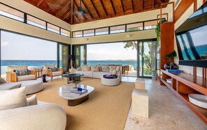 Ampla sala de estar com uma grande janela com vista para o mar, equipada com sofás e uma mesa de centro.