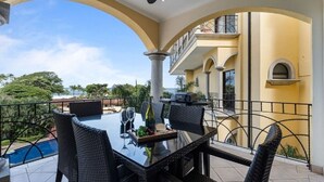 Ein überdachter Essbereich im Freien mit Tisch, Stühlen, einem Grill und Blick aufs Meer.
