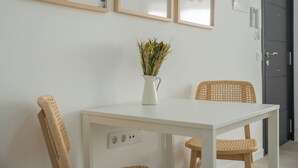 Ett vitt bord med en vas med torkade växter, två flätade stolar och inramad väggkonst som föreställer fiskar och vågor.