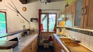 Eine schmale Küche mit Holzausstattung, einem eingebauten Ofen und einem Fenster mit Vorhängen.