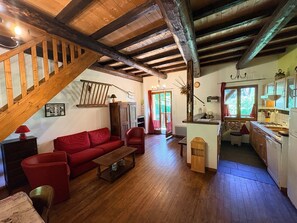 Un intérieur rustique avec un escalier en bois, un canapé rouge, une table basse en bois et un coin cuisine équipé d’un évier et d’une cuisinière.