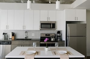 A modern kitchen with white cabinets, stainless steel appliances, and a central island with two wine glasses and a potted plant.