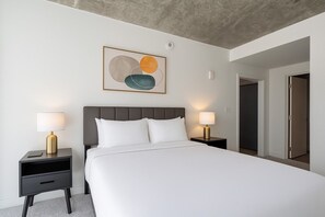 A hotel room with a large bed, two bedside tables with lamps, a modern abstract painting, and a concrete ceiling.