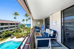 Ein Balkon mit Pool, Gartenmöbeln und Blick auf das Meer und Palmen.