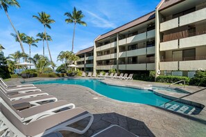 A hotel with a swimming pool, lounge chairs, palm trees, and a multi-story building. - Across From Magic Sands Top Floor Condo w/ AC (Kailua-Kona)
