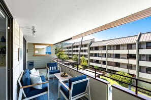 A balcony with a sofa, chairs, and a table with fruit. - Across From Magic Sands Top Floor Condo w/ AC (Kailua-Kona)