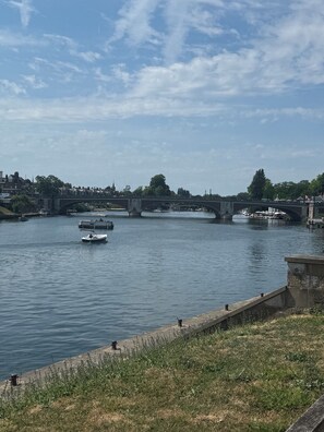 A river with boats, a bridge, and a grassy bank. - Charming riverside apartment (Hampton)