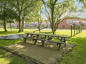 Ein Picknicktisch in einem Park mit Trampolin, Bäumen und einem Spielplatz im Hintergrund.