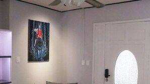Quarto com ventilador de teto, porta com painel de vidro fosco, pintura na parede, planta em vaso e chão xadrez.
