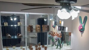 Uma sala de jantar com uma mesa redonda, cadeiras, uma vitrine de vidro com objetos decorativos e um ventilador de teto.