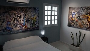 Quarto com cama, janela e duas grandes pinturas abstratas nas paredes.