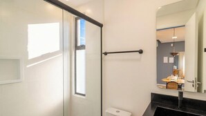 Ein modernes Badezimmer mit Duschkabine aus Glas, Toilette, schwarzem Waschtisch und großem Spiegel.