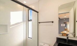Ein modernes Badezimmer mit Duschkabine aus Glas, Toilette, schwarzem Waschtisch und großem Spiegel.