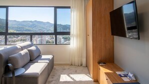 Ein modernes Hotelzimmer mit einer Couch, einem Schreibtisch, einem Flachbildfernseher und einem großen Fenster mit Blick auf die Stadt.