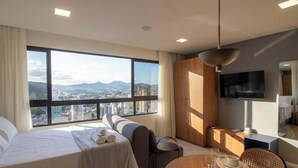 Ein modernes Hotelzimmer mit großem Fenster, einem Bett, einer Couch, einem Essbereich und einem Fernseher.