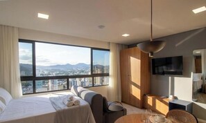 Ein modernes Hotelzimmer mit großem Fenster, einem Bett, einer Couch, einem Essbereich und einem Fernseher.