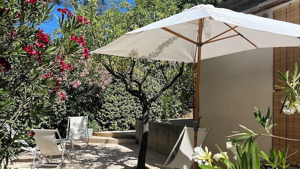 Une terrasse extérieure avec un parasol blanc, deux chaises longues blanches et un sol en béton.