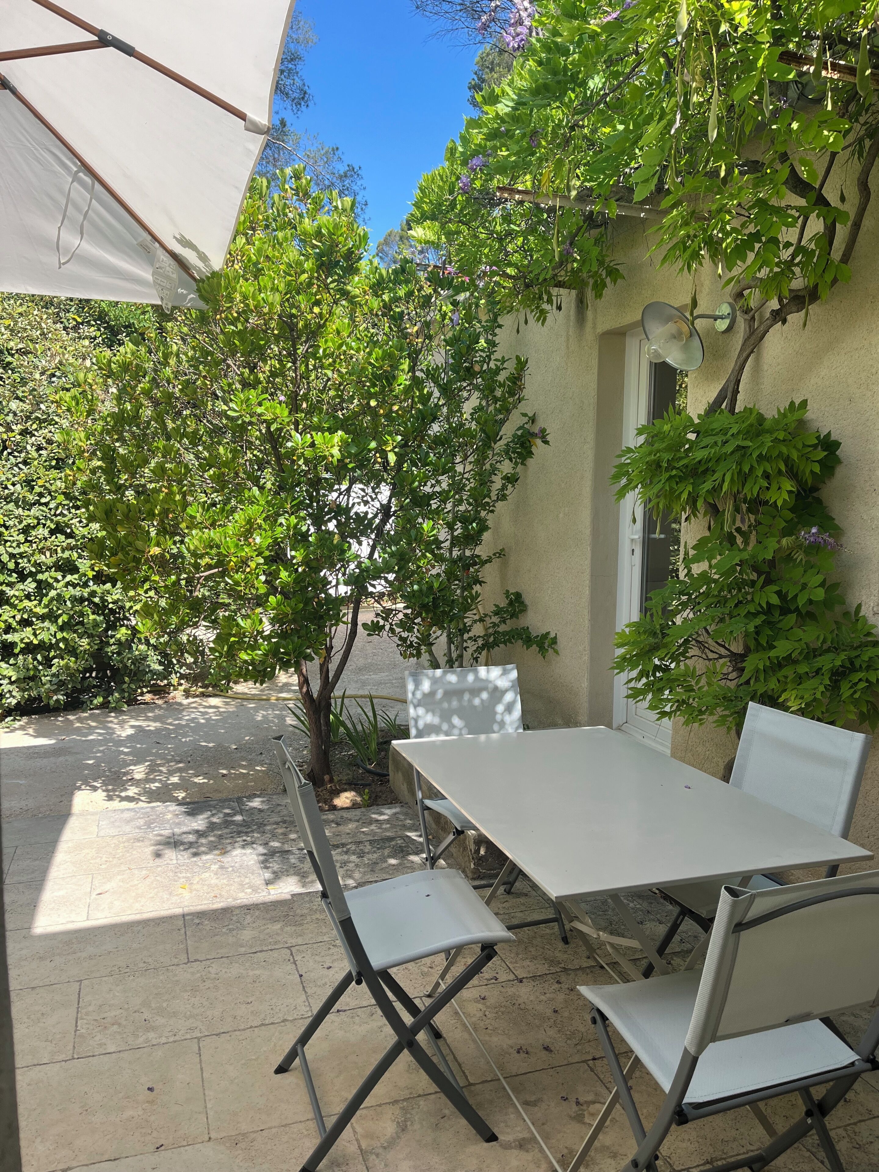 Een terras buiten met een tafel en stoelen, omringd door groen en een witte parasol.