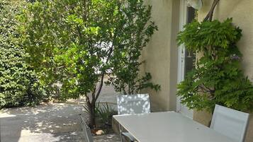 Een terras buiten met een tafel en stoelen, omringd door groen en een witte parasol.