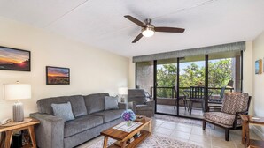 A living room with a gray sofa, a wooden coffee table, a ceiling fan, and a large sliding glass door leading to an outdoor patio. - Walk to Historic Kailua Village Kona Pacific C317 w/ A/C & Large Lanai (Kailua-Kona)