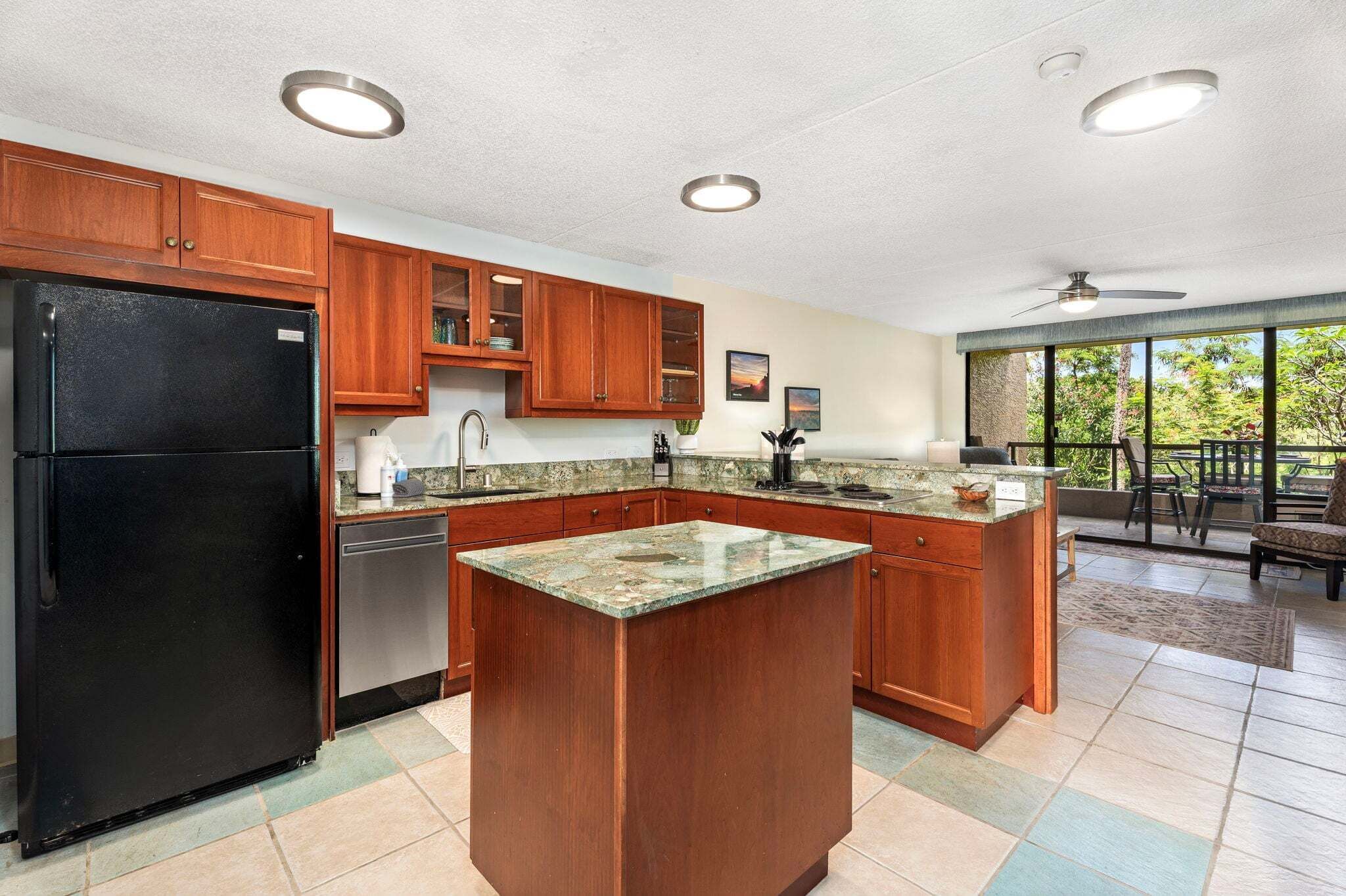 Cocina con armarios de madera, un refrigerador negro, encimeras de granito y una isla grande.