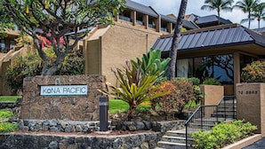 A building with a sign reading 'KONA PACIFIC,' a stone wall, and a staircase leading to the entrance. - Walk to Historic Kailua Village Kona Pacific C317 w/ A/C & Large Lanai (Kailua-Kona)