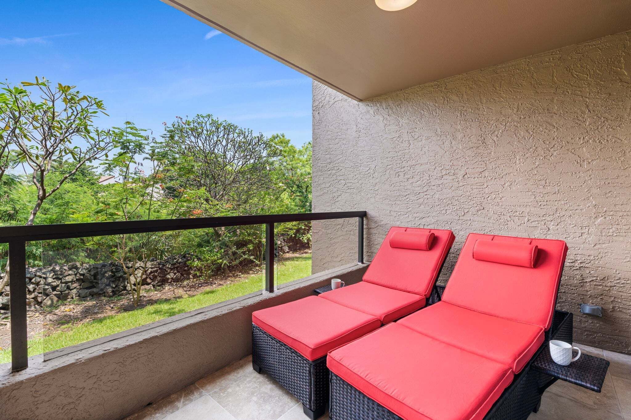Un balcon avec deux fauteuils de relaxation rouges dotés de coussins, un mur en pierre et une vue sur la verdure.
