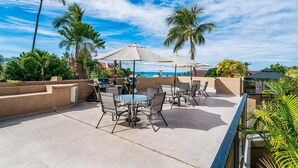 An outdoor patio with tables and chairs, surrounded by palm trees and a clear sky. - Walk to Historic Kailua Village Kona Pacific C317 w/ A/C & Large Lanai (Kailua-Kona)