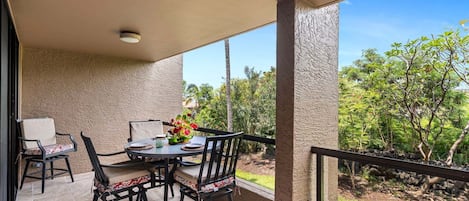 Um alpendre coberto com mesa e cadeiras, um arranjo floral e vista para o verde.