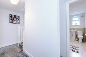 Ein Flur, der zu einem Badezimmer führt, mit einer weißen Wand, einem gerahmten Tigerbild und einer Treppe.