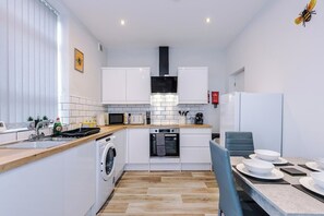 Eine kompakte Küche mit Waschmaschine, Mikrowelle und Backofen, sowie eine Essecke mit Tisch für vier Personen.