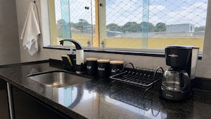 A kitchen with a granite countertop, a stainless steel sink, a coffee maker, and three black containers labeled 'Café,' 'Acucar,' and 'Sal.'