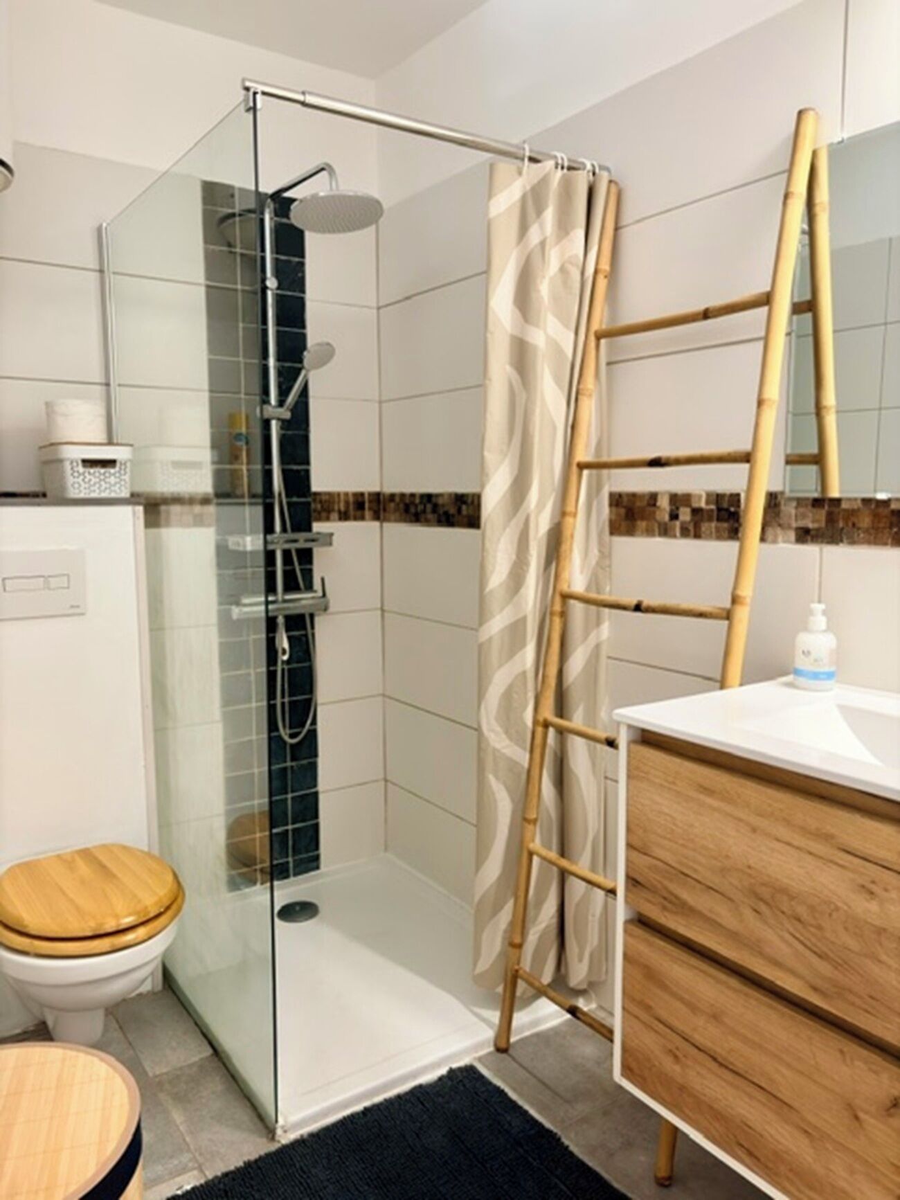 Een badkamer met een douchecabine van glas, een toilet, een wastafel met spiegel en een houten kruk.