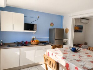 A compact kitchen with a microwave, refrigerator, and a dining area with a table and chairs. - Small sandy beach with a pool and ocean view at Anse Mitan (Les Trois-Îlets)