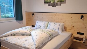 Een houten bed met hoofdeinde, een nachtkastje, een kunstwerk aan de muur en een raam met uitzicht op een bouwplaats.