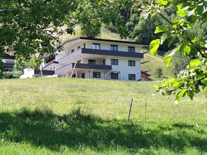 A modern two-story house with a balcony, surrounded by a grassy field and trees. - Aussichtsplatz Apartment (Laimach)