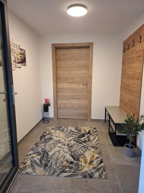 A hallway with a wooden door, a patterned rug, a small table with a plant, and a wall-mounted coat rack. - Aussichtsplatz Apartment (Laimach)
