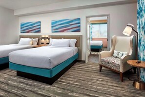 Ein Hotelzimmer mit zwei Betten, einem Sessel, einer Lampe und abstrakten Wandbildern.