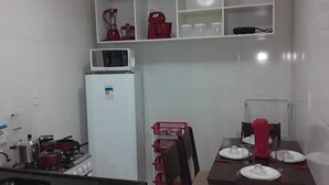 A compact kitchen with a stove, microwave, and dining table set for two. - FLATS CABANOS (Maragogi)