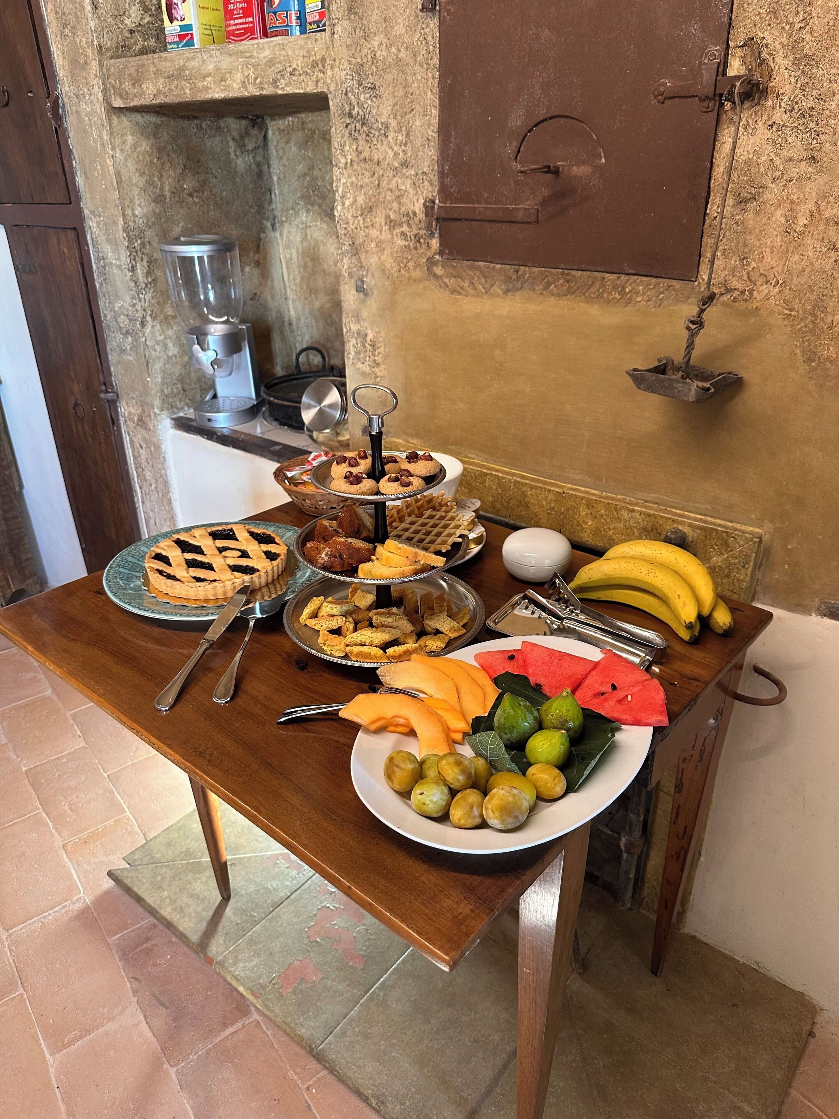 A table with various food items, a coffee machine, and a rustic wall.