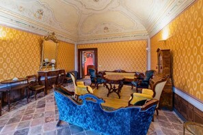 Une pièce avec un papier peint à motifs, un canapé bleu, des meubles en bois et un miroir.