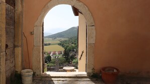 An arched doorway leading to a balcony with a view of a village and mountains.