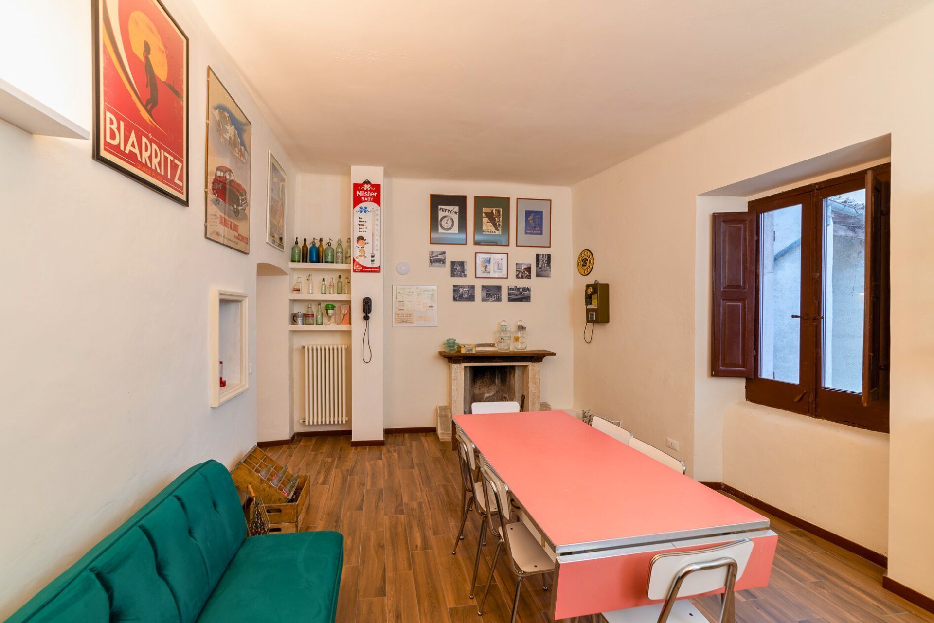 Una habitación con una mesa de comedor, sillas, un radiador, una chimenea y varias imágenes enmarcadas en las paredes.