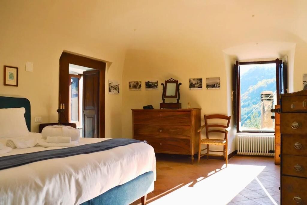 Une chambre à coucher avec un lit, une commode en bois, une chaise et une fenêtre donnant sur la montagne.