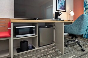 Ein Hotelzimmer mit Schreibtisch, Mikrowelle, Minikühlschrank, einem roten Sessel, einer Lampe und Teppichboden.