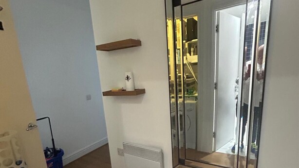A room with a mirrored closet door, a radiator, and two wooden shelves with items on them. - Sleeps4-familyfriendly-kingbeds-2bath (London)