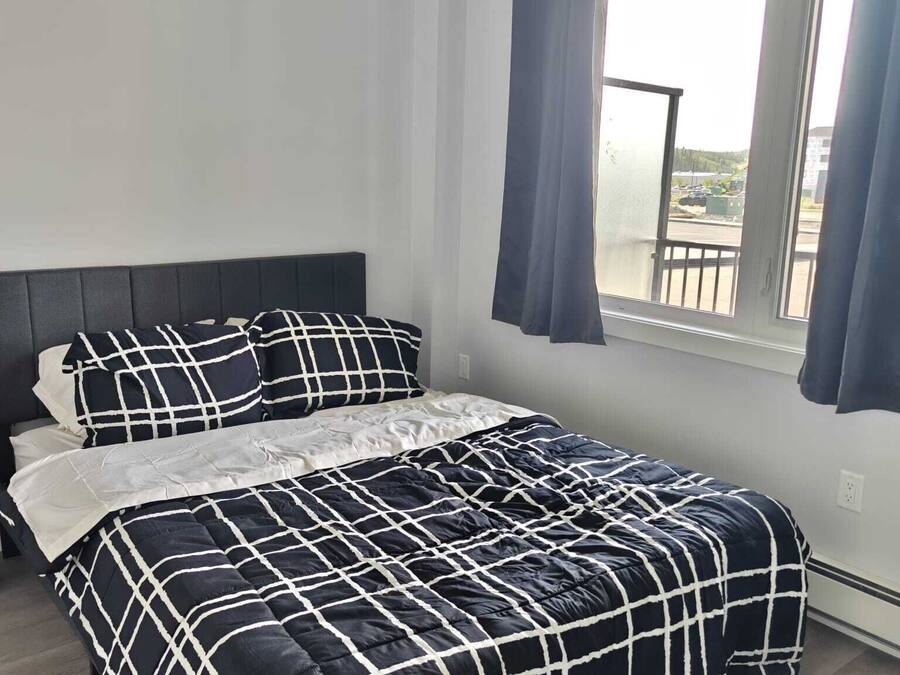 A bed with a black and white checkered bedspread, a dark headboard, and a window with curtains.