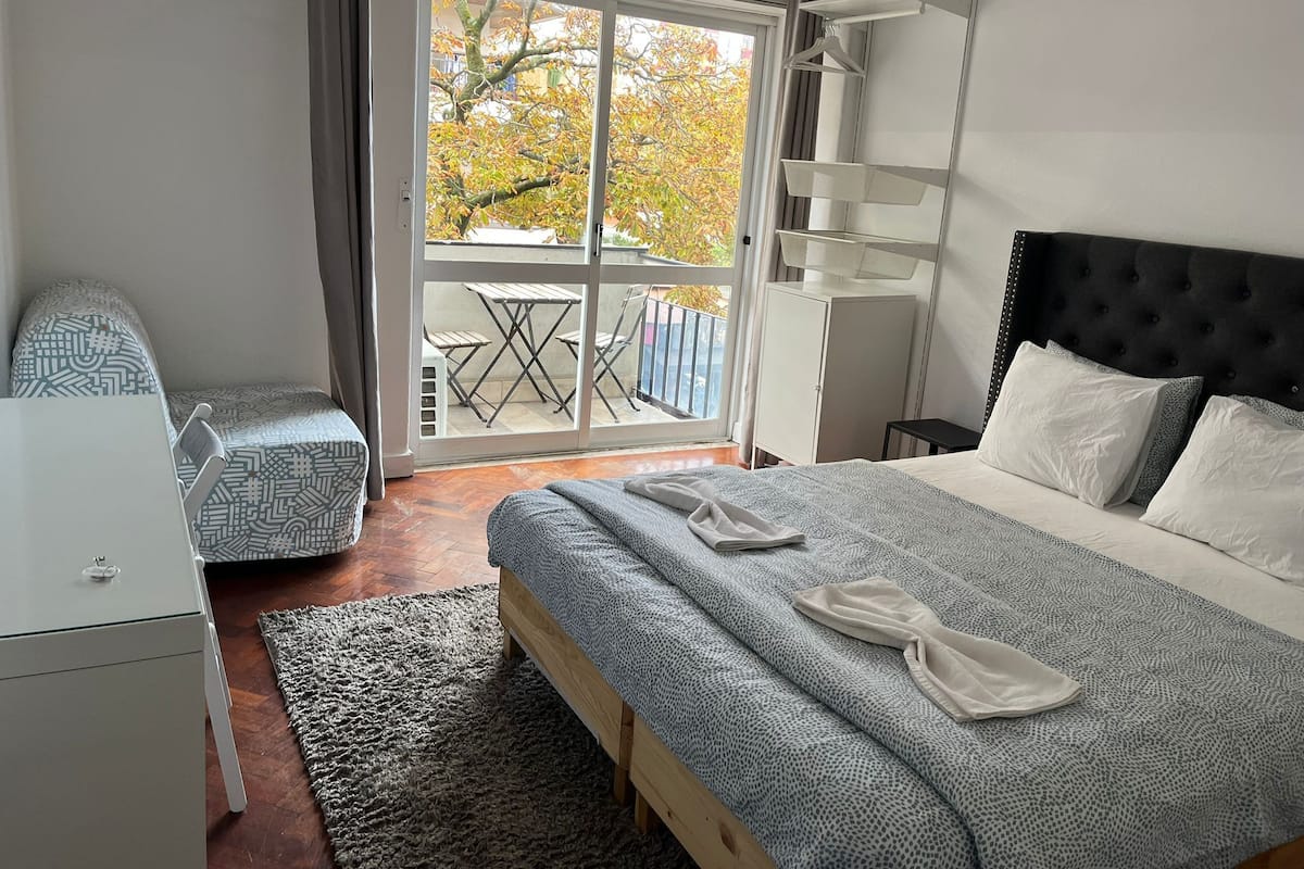 Una habitación de hotel con cama, una silla, un escritorio y un balcón con mesa y sillas.