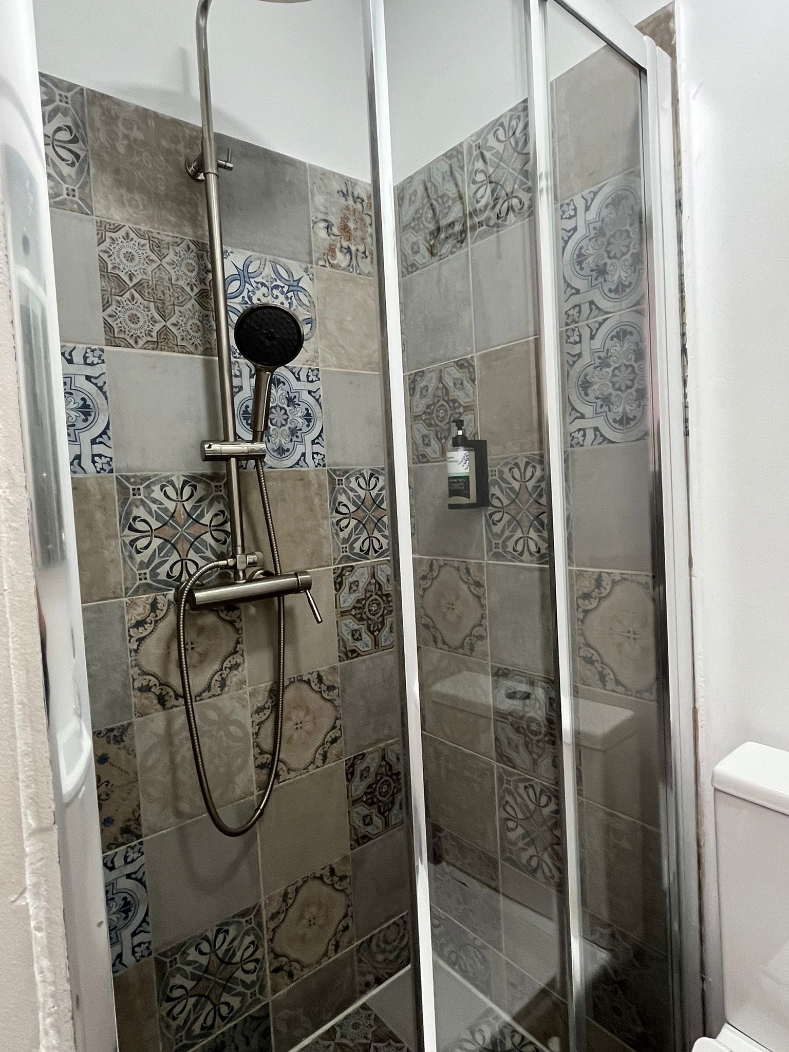 A shower with a glass door, patterned tiles, and a handheld showerhead.