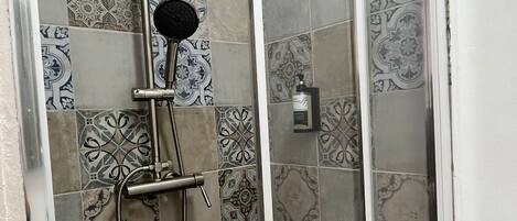 A shower with a glass door, patterned tiles, and a handheld showerhead.